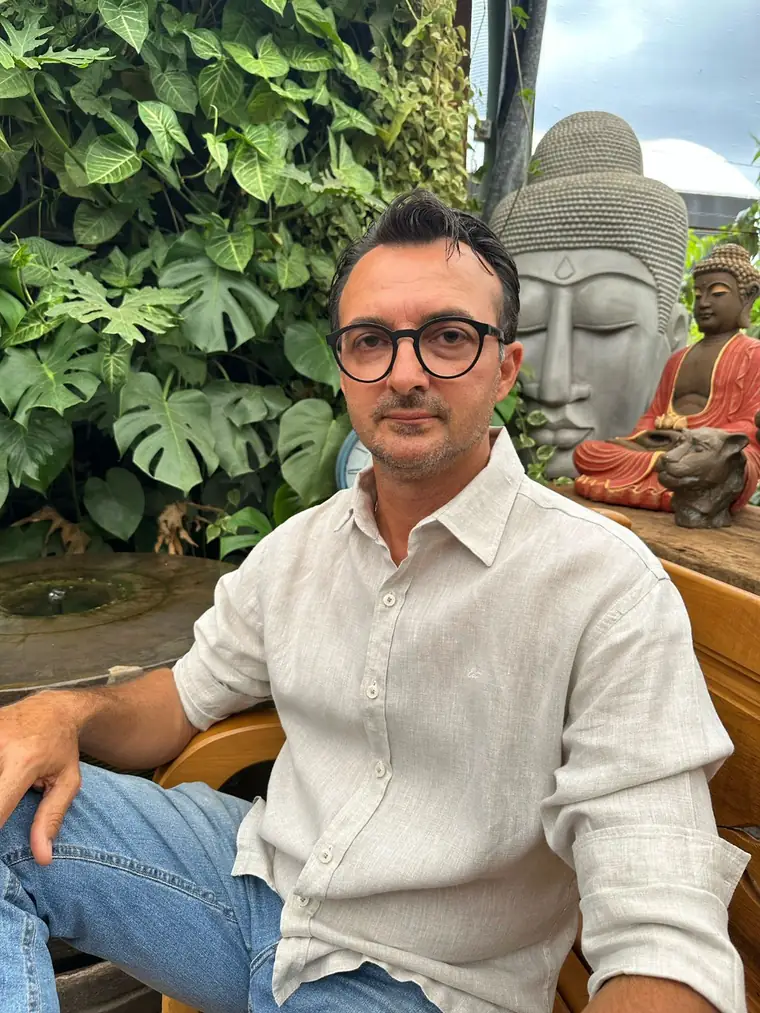 Douglas Zaneti sentado em frente a uma parede de folhagens e a uma escultura de Buda, na loja da Plant Garden
