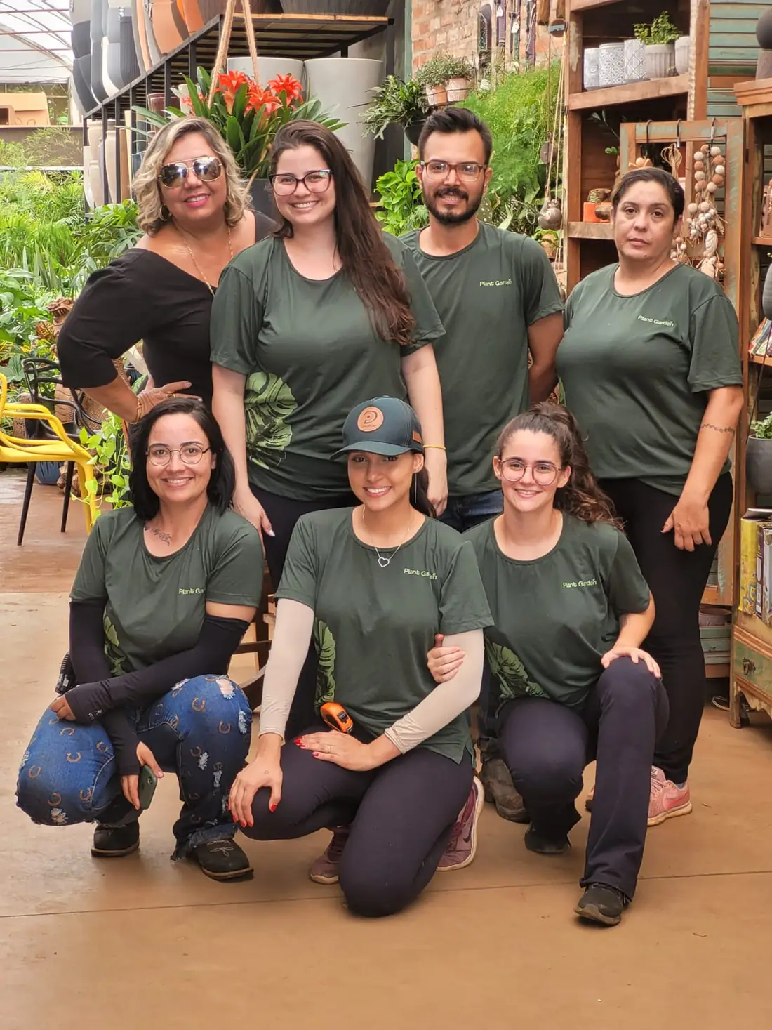 Equipe da Plant Garden Paisagismo reunida dentro da loja, oito pessoas de camiseta verde-escura do uniforme