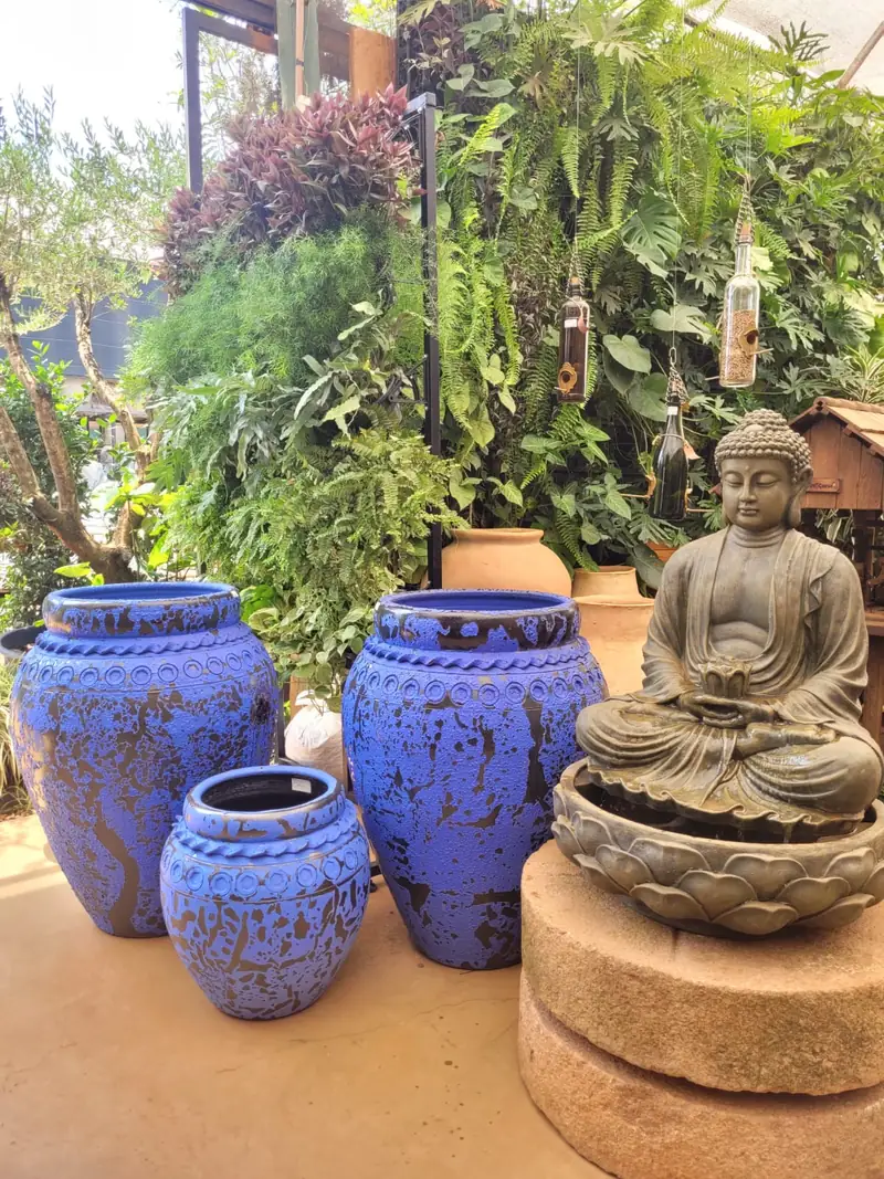 Três vasos vietnamitas de cerâmica esmaltada em azul cobalto e uma escultura de Buda, expostos no pátio da loja